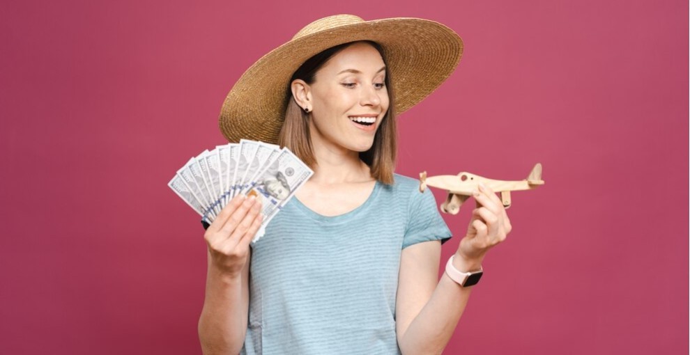 Mulher segurando cédulas de dólar em uma mão e um avião de brinquedo na outra